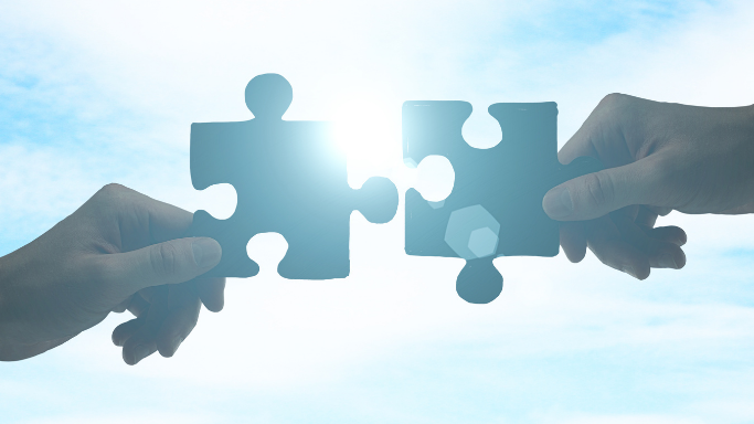 Two hands holding puzzle pieces that fit together, representing aligned financial services and solutions